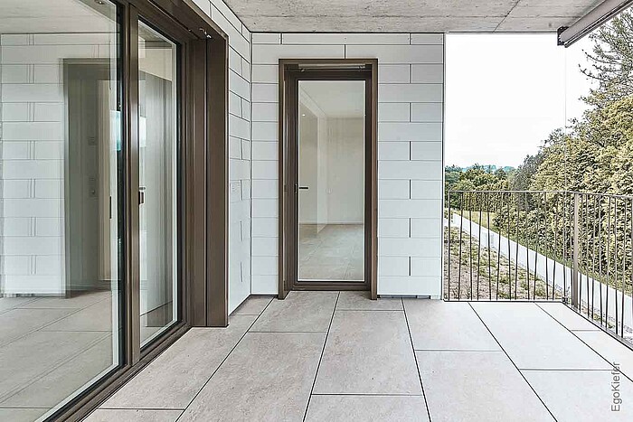 Aussenaufnahme, überdachte Terrasse mit Fliesenboden, links sind grosse Hebeschiebetüren sichtbar 