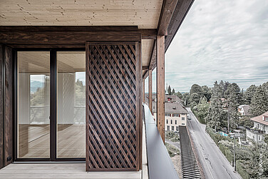 Moderne Holzfassade mit Schiebeladen vor einer großen Glas-Schiebetür auf einem Balkon mit Ausblick