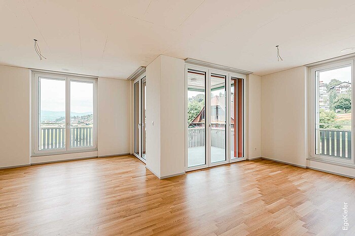 Spazio abitativo luminoso e vuoto con pavimento in parquet e finestre in PVC-U EgoKiefer a tutta altezza nel complesso “Scheidegg”.