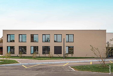 Frontale Ansicht des modernen, zweigeschossigen Schulgebäudes Bellicot mit symmetrisch angeordneten Fenstern und neu angelegtem Aussenbereich.