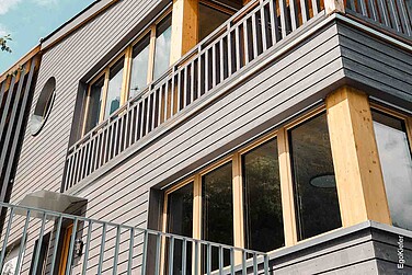 Détail de la façade de la maison jumelée « zum Pulverturm » à Schwanden avec revêtement en bois lambrissé et fenêtres modernes en bois