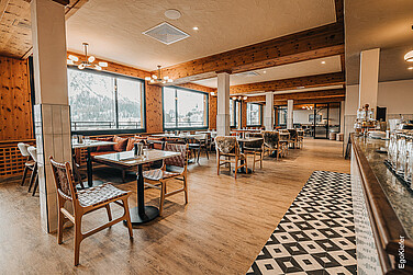 Innenaufnahme im Panoramic Restaurant des Alpenresort FAERN in Arosa, links eine ganze Front grosser Holz/Aluminium-Fenster mit Blick auf die Berge und stilvoller Einrichtung