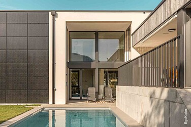Glasfassade mit schwarzem Rahmen, angrenzender Terrasse und Poolbereich.