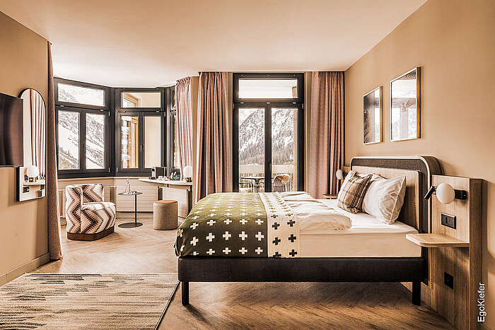 Innenaufnahme eines Zimmers, welches dank der grossen EgoKiefer Holz/Aluminium-Fenster sehr hell wirkt und eine schöne Aussicht nach Draussen bietet
