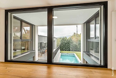 Moderne, grosse Holz/Aluminium-Fenster EgoAllstar mit schwarzem Rahmen, die festverglast sind und einen Blick auf einen Aussenbereich mit Pool, Terrasse und Garten freigeben
