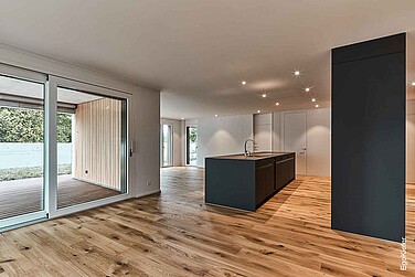 Innenaufnahme der Residence Lueg, modernes, offenes Wohnzimmers mit grossen EgoKiefer Fenstern und Zugang zur Terasse