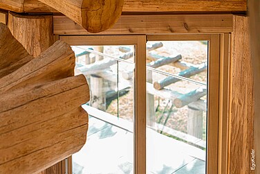 Innenansicht des Blockhauses mit einer Holz-Hebeschiebetüre im Bild, welche sich harmonisch in die natürliche Holzarchitektur integriert und Ausblick auf die Terrasse zeigt.