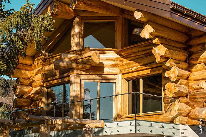 Detailansicht eines Blockhauses in Amden, Schweiz, mit massiver Holzbauweise und Holzfenstern des Typs EgoWoodstar, die sich harmonisch in die rustikale Architektur einfügen.