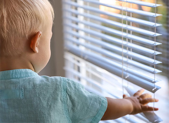 Kleiner Junge berührt die Innenjalousien